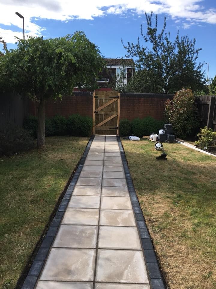A paved path running down a lawned garden to a timber gate.