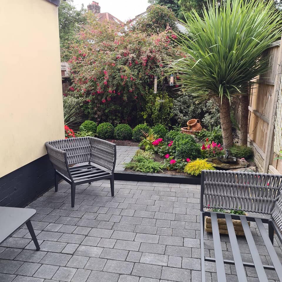 A block-paved seating area with garden furniture, planted borders and a palm.