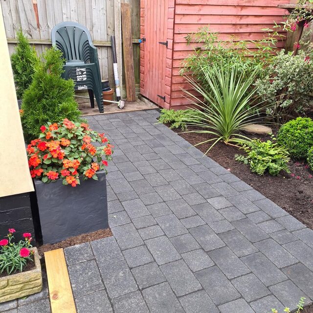 A block-paved side area with planters of bedding and architectural shrubs.