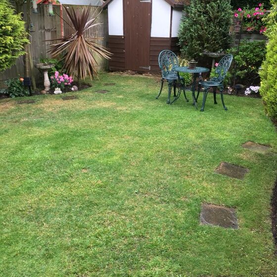 A cut lawn with stepping stones, planted edges and a garden table.